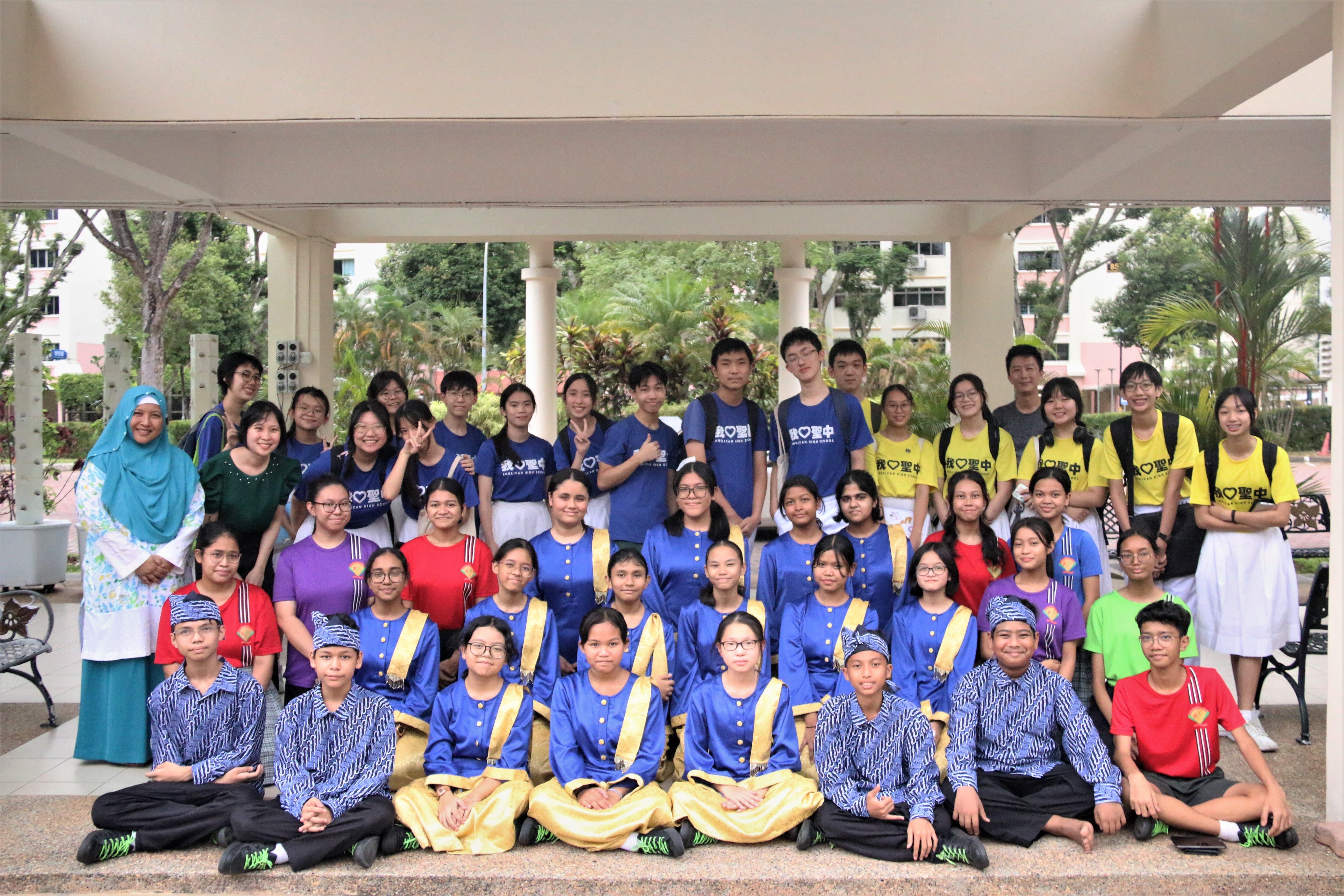 Group of students and teachers posing under a covered walkway, some in blue-and-gold and sports uniforms.